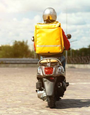 Fast Food Delivery. Courier Man Riding Scooter Delivering Meals From Restaurants With Yellow Bag Driving Outdoors. Back View, Copy Space